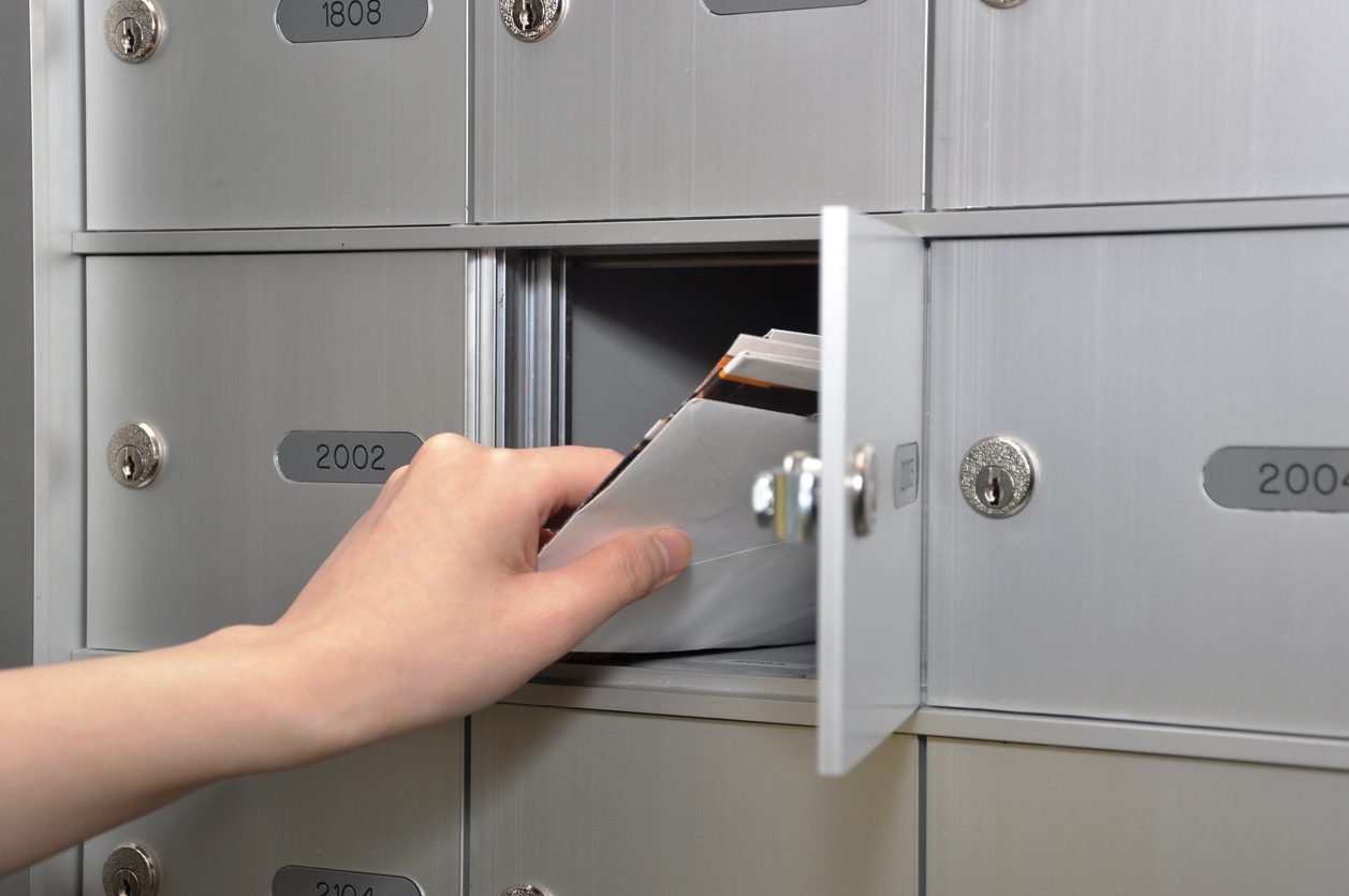 Direct mail is a great way to engage your audience. Image: A hand taking envelopes out of a community mailbox.
